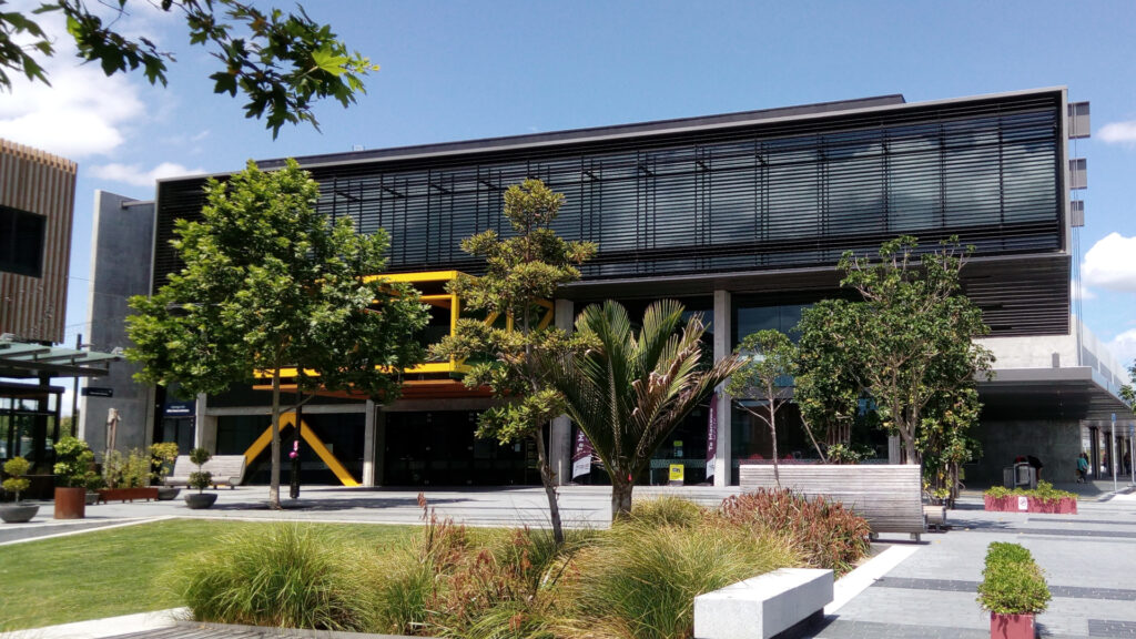 Te Manawa (Westgate Library and Multi-Purpose Facility) facade with trees & a small park in the foreground.